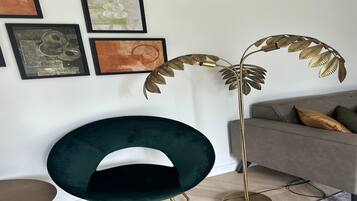 A modern living room with a dark green chair, a gold floor lamp, and a grey sofa with cushions.