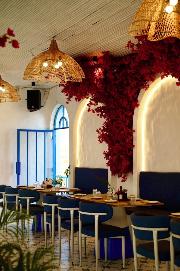 Un restaurante con sillas azules, una mesa de madera y un techo con lámparas de fibra trenzada.