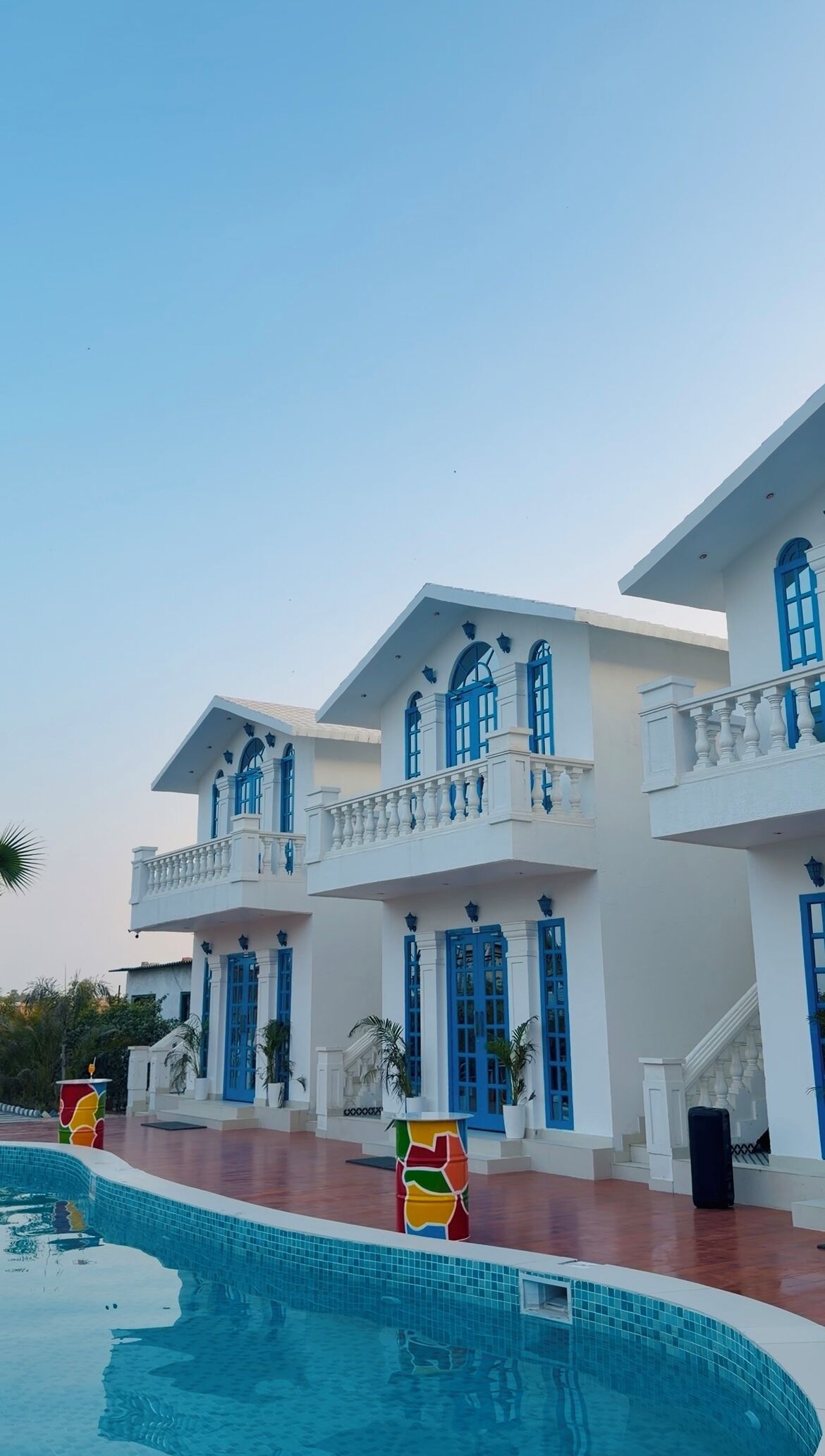 A large, white building with blue accents and a swimming pool in front.