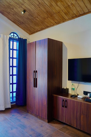 Habitación con techo de madera, un amplio armario, televisor de pantalla plana y una ventana con cortinas azules.