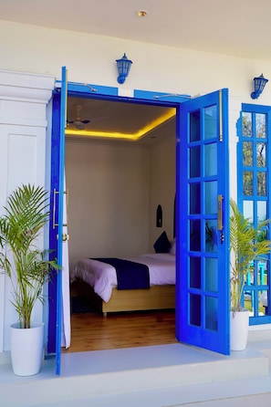 A room with a bed, a blue door, and a potted plant.