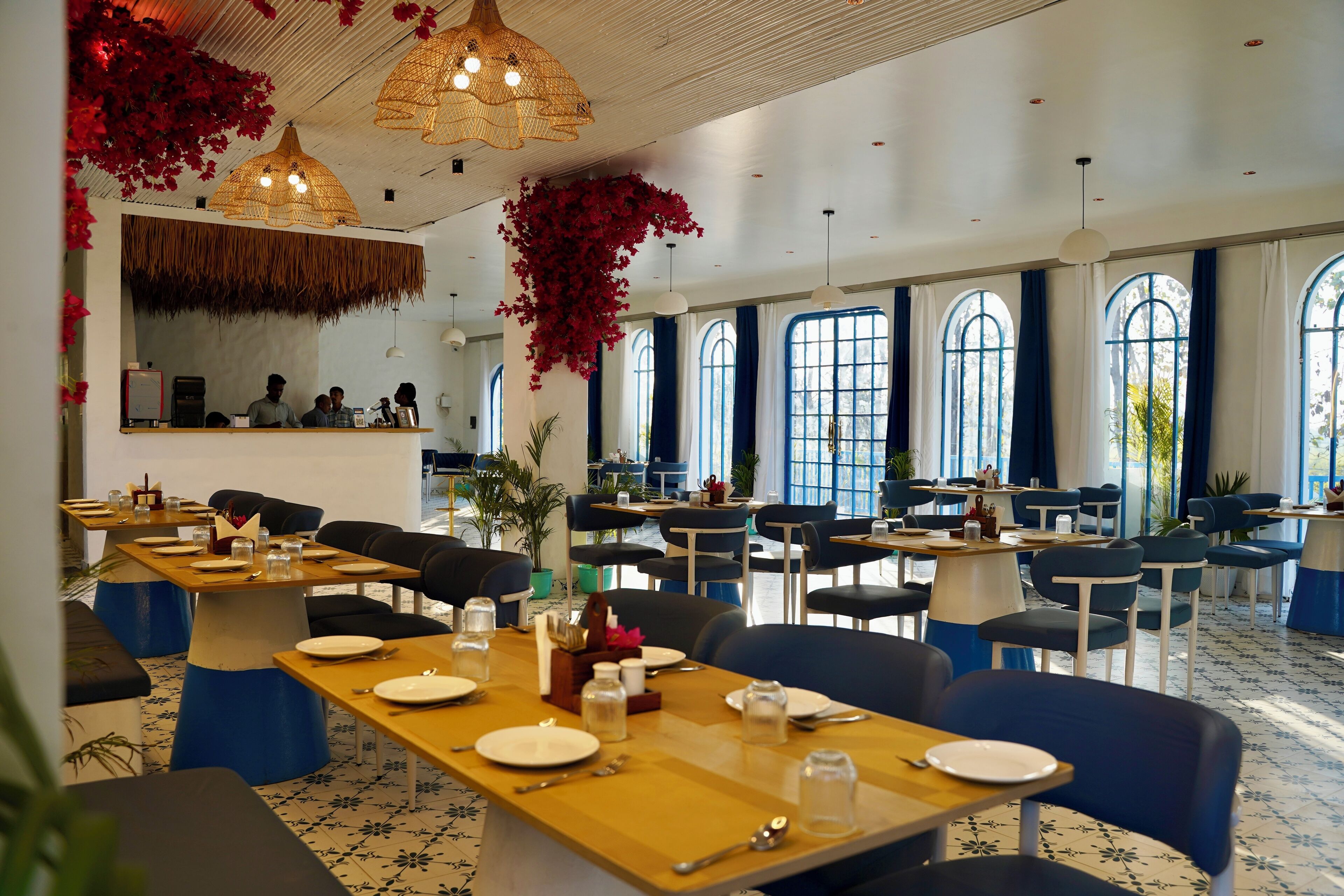 A restaurant with multiple dining tables, chairs, and hanging red flowers.