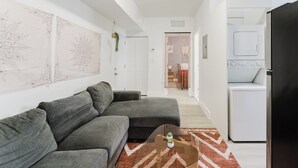 Ein modernes Wohnzimmer mit einem grauen Ecksofa, einem Glastisch und einem gemusterten Teppich.