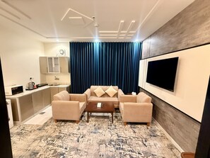 Ein modernes Wohnzimmer mit einer Sofagarnitur, einem Couchtisch, einem flachbildfernseher an der Wand und einem Küchenbereich im Hintergrund.