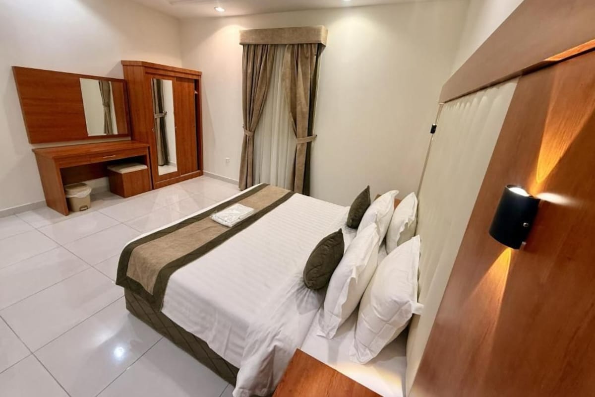 Quarto de hotel com cama, guarda-roupa, espelho e janela com cortinas.