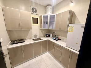 A compact kitchen with a built-in microwave, a sink, and a refrigerator. - Milestone Rise Serviced Apartments (Jeddah)