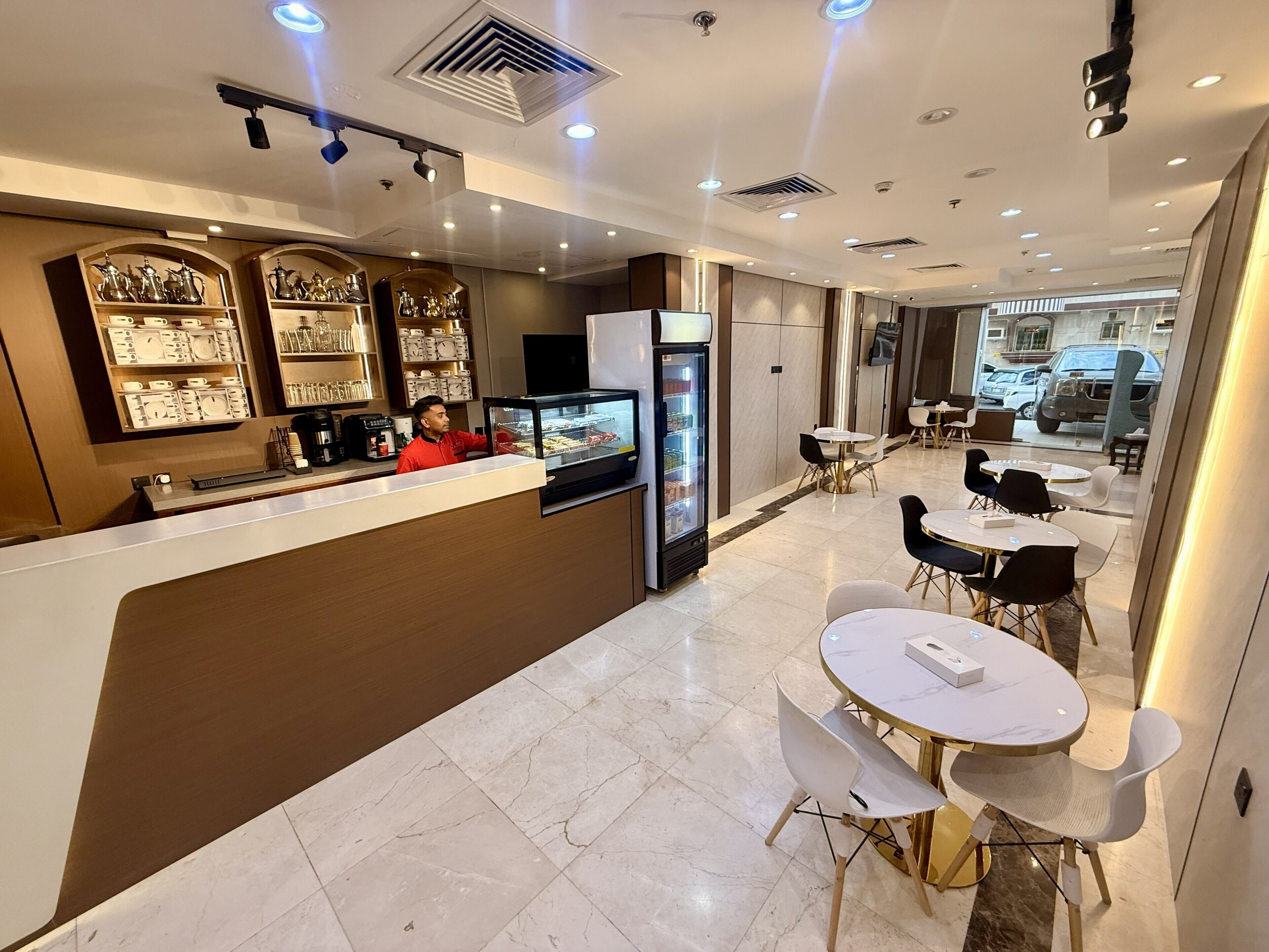 A modern hotel lobby with a reception desk, seating area, and a view of the street.