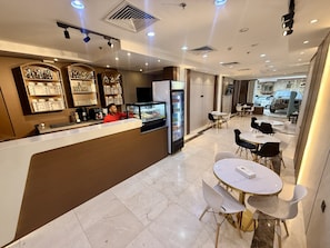 A modern hotel lobby with a reception desk, seating area, and a view of the street.