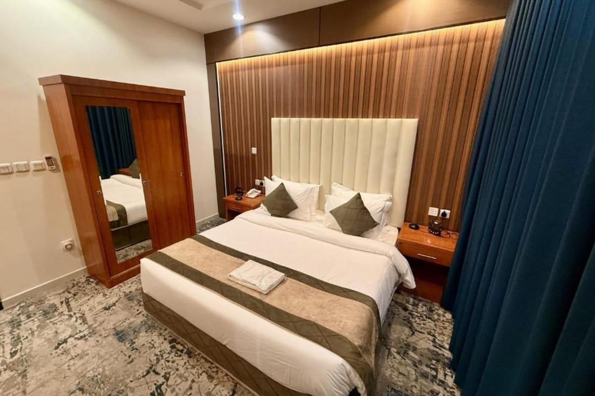 Quarto de hotel com uma cama grande, cabeceira de madeira, mesa de cabeceira e um espelho.
