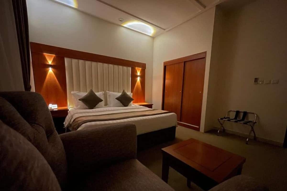 Habitación de hotel con cama, lámparas de noche, cabecera de madera, banco de madera y una mesita.