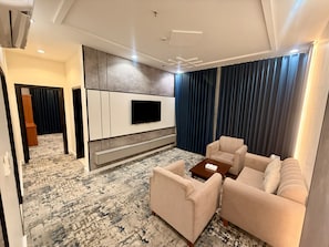 A modern living room with a flat-screen TV mounted on a wall, a patterned carpet, a beige sofa, and a coffee table.