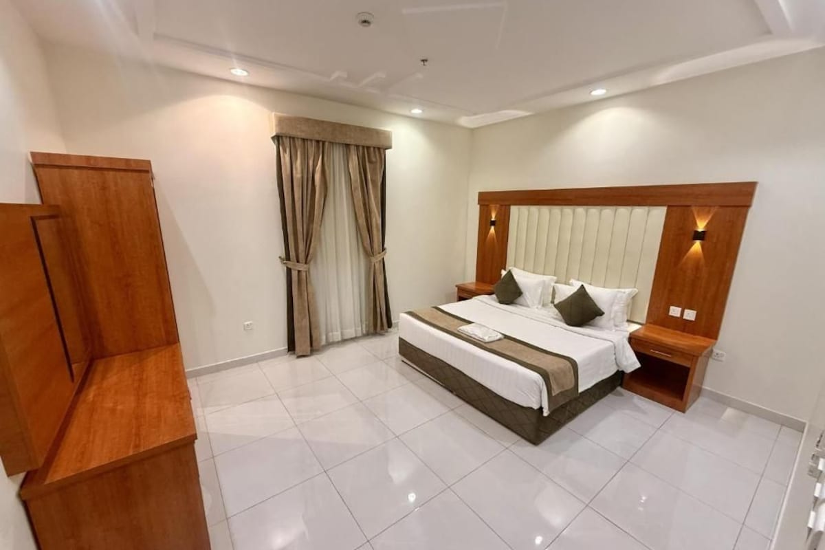 Quarto de hotel com uma cama grande, um guarda-roupa de madeira, uma mesa de cabeceira e uma cortina.