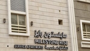 Ein Gebäude mit einem Schild, auf dem 'MILESTONE RISE SERVICE APARTMENTS' in Arabisch und Englisch steht.