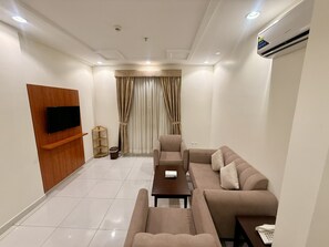 A modern living room with a flat-screen TV mounted on a wooden panel, a sofa set, a coffee table, and a small side table with a telephone. - Milestone Rise Serviced Apartments (Jeddah)
