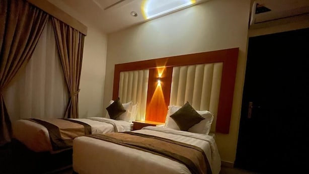 Ein Hotelzimmer mit zwei Betten, einem großen Fenster mit Jalousien, einer Deckenlampe und einer Tür.