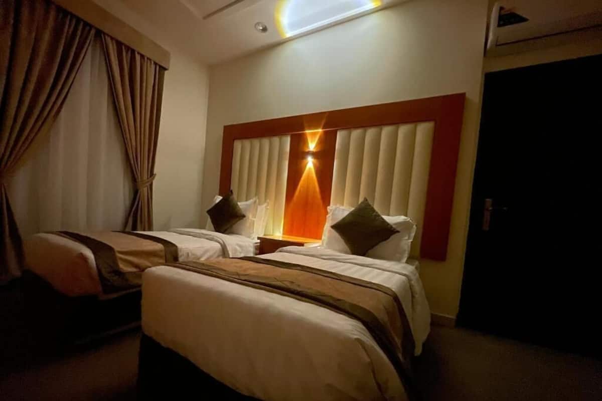 Una habitación de hotel con dos camas, un ventanal con persianas, una lámpara en el techo y una puerta.