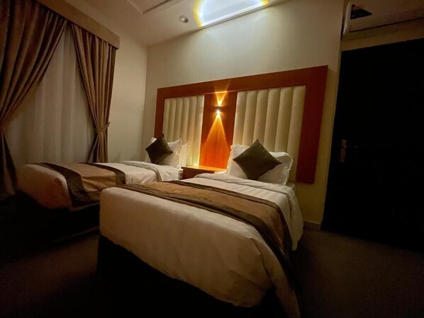 A hotel room with two beds, a large window with blinds, a ceiling light, and a door. - Milestone Rise (Jeddah)