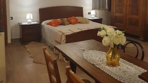 A bedroom with a wooden bed, a nightstand with a lamp, a chandelier, a wooden wardrobe, and a dining table with chairs. - Il Castelletto di Gomo  (Godiasco)