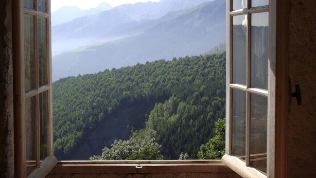 A room with a large window offering a view of a forested valley and distant mountains.