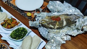 A table with a whole fish in foil, accompanied by various side dishes.