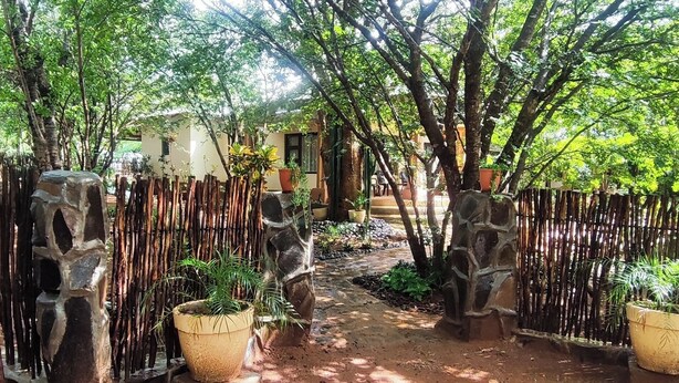 A pathway flanked by bamboo fencing and potted plants, leading to a building with a tiled roof.