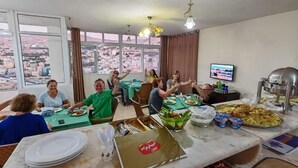 Eine Gruppe von Menschen speist in einem Raum mit großen Fenstern, die auf eine Stadtlandschaft blicken.