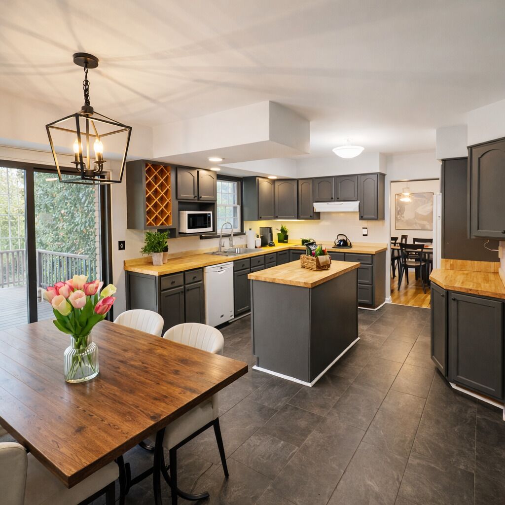Una cocina moderna con armarios oscuros, una isla de madera y un comedor con mesa y sillas.