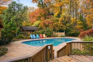 Un jardin avec une piscine, une terrasse en bois et des fauteuils Adirondack.