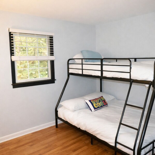 Une chambre avec un lit superposé, une fenêtre, un plancher en bois et un oreiller orné d’un motif.