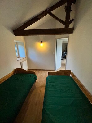 A small, narrow room with two wooden beds, a sloped ceiling, and a single light fixture.