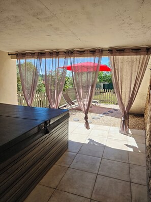 A covered outdoor area with a dark-colored bench, a white picket fence, and a red umbrella in the background. - Gîte Les Voûtelettes (Saint-Jean-de-Ceyrargues)