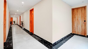 A hallway with a marble floor, wooden doors, and potted plants. - Townhouse Oak Sector 18 Metro Station (Noida)