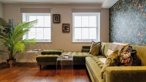 A living room with a green sofa, a clear coffee table, a potted plant, and a large window with a view. - Stunning High Street Loft in Cheltenham (Cheltenham)