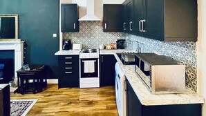 Une cuisine moderne avec des meubles de couleur sombre, un îlot central, un four encastré et un luminaire suspendu.