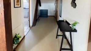 Un pasillo con techo de madera, una mesa negra con un florero y un cuadro en la pared.