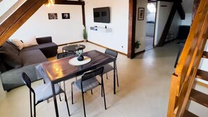 Un espacio tipo loft con mesa de comedor, sillas, sofá y televisor montado en la pared.