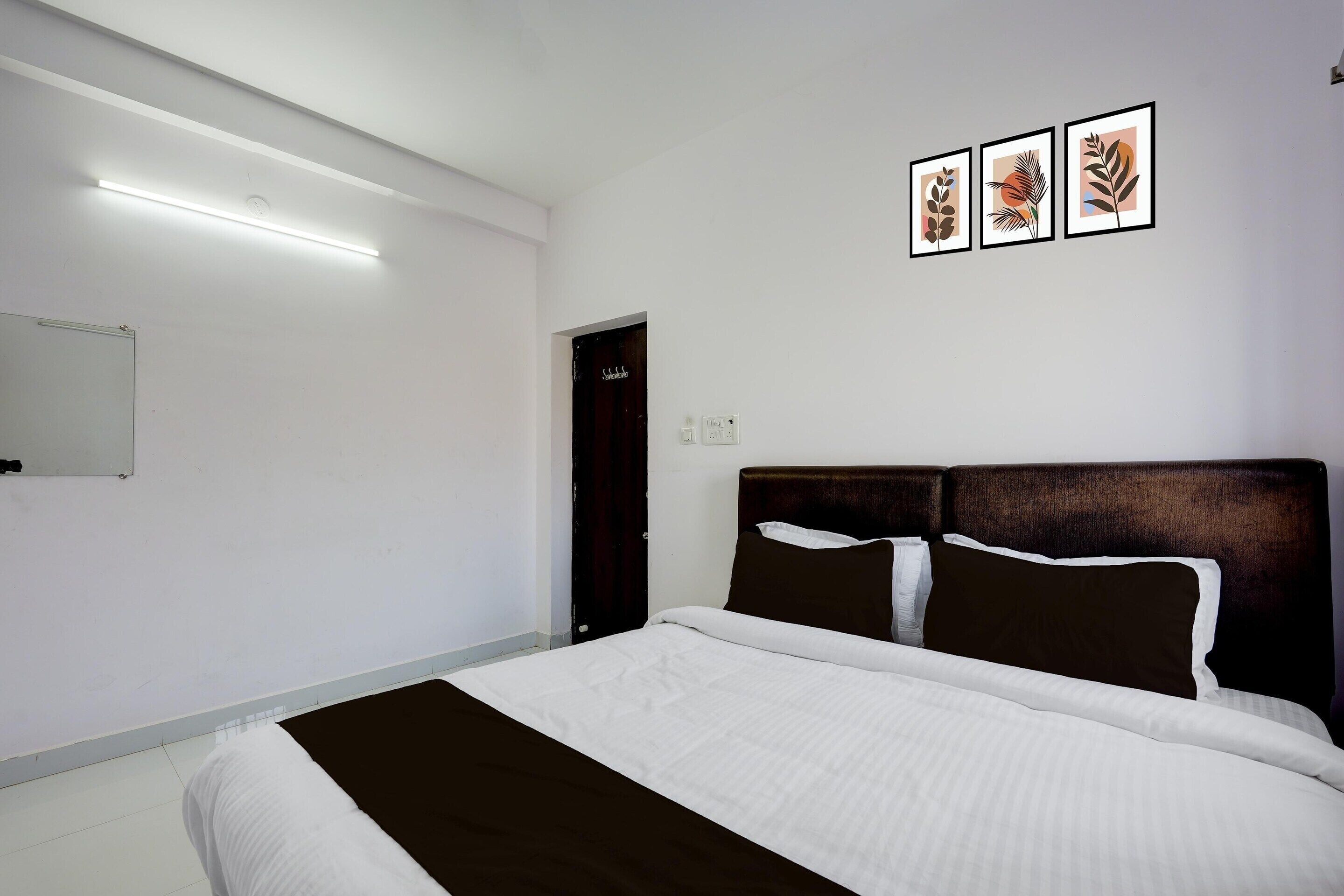 Una cama bien tendida con una colcha blanca y marrón, un cabecero oscuro y tres láminas enmarcadas con motivos botánicos en la pared.