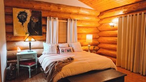 Une chambre confortable dans un chalet en rondins, avec un lit en bois, deux lampes de chevet, un banc et un tableau accroché au mur.
