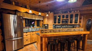 Une cuisine dotée de meubles en bois, d’un réfrigérateur en acier inoxydable, d’un comptoir-bar avec des tabourets et de luminaires suspendus.