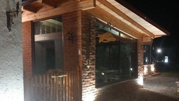 A building with a wooden pergola, brick walls, and a gravel driveway at night.