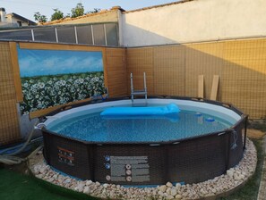 A round above-ground pool with a ladder, surrounded by a pebble border, and a mural of a flower field on the adjacent wall. - Intimate and cozy cottage with garden and whirlpool for exclusive use. (Castel del Bosco)