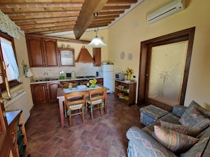 A cozy kitchen with wooden cabinets, a dining table with chairs, and a patterned sofa. - Intimate and cozy cottage with garden and whirlpool for exclusive use. (Castel del Bosco)