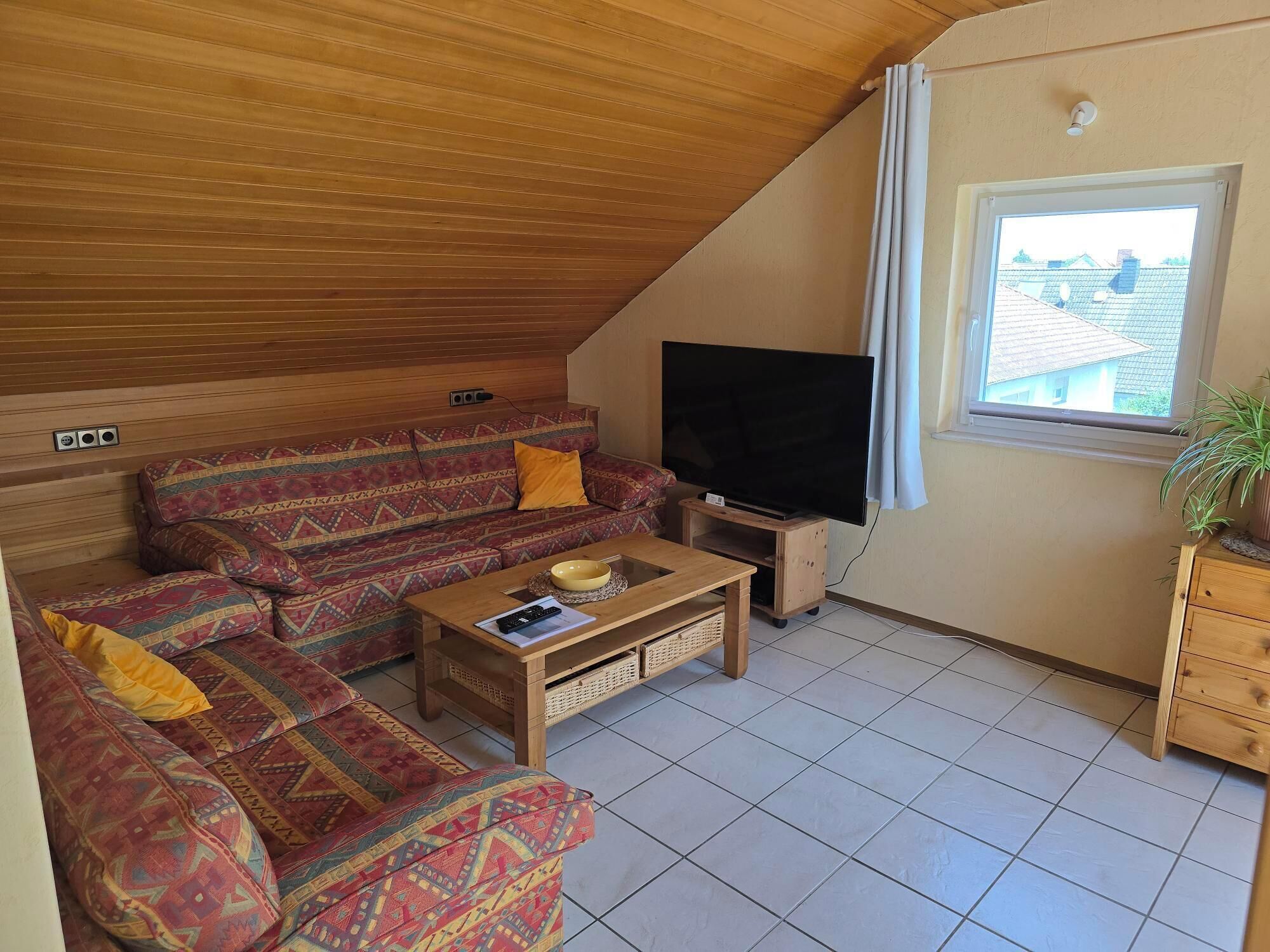 A cozy living room with a sofa, a coffee table, a TV, and a window with curtains.