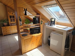 Una cocina compacta con armarios de madera, un microondas, una cafetera y un refrigerador pequeño.