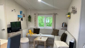 Een woonkamer met een bank, poef, tafel en een televisie op een standaard.