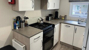 Een kleine keuken met een gasfornuis, oven, witte kasten, een koffiezetapparaat en een raam met uitzicht.