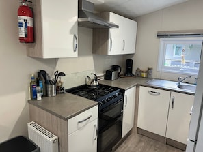 A compact kitchen with a gas stove, oven, white cabinets, a coffee maker, and a window with a view. - Chalet JT 08 - Time out near the sea, Renesse (Renesse)