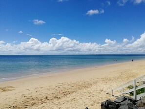 Uma praia com céu claro, areal arenoso e uma grade.
