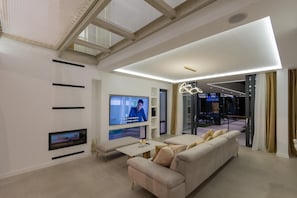 Uma sala de estar moderna com uma grande TV de tela plana, um sofá e um vidro que dá para uma varanda.