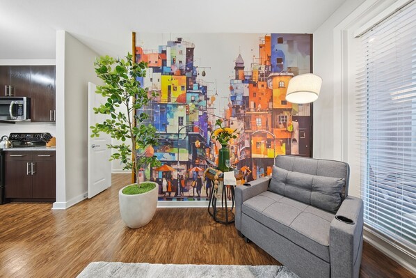 Uma sala de estar moderna com um sofá cinzento, um quadro abstrato grande, um vaso de planta e piso de madeira.
